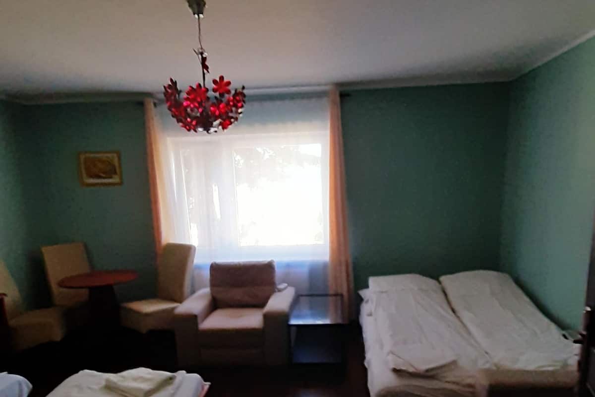 Ein Hotelzimmer mit zwei Einzelbetten, einem kleinen Tisch, zwei Stühlen, einer Pendelleuchte und einem fenster mit Vorhängen.