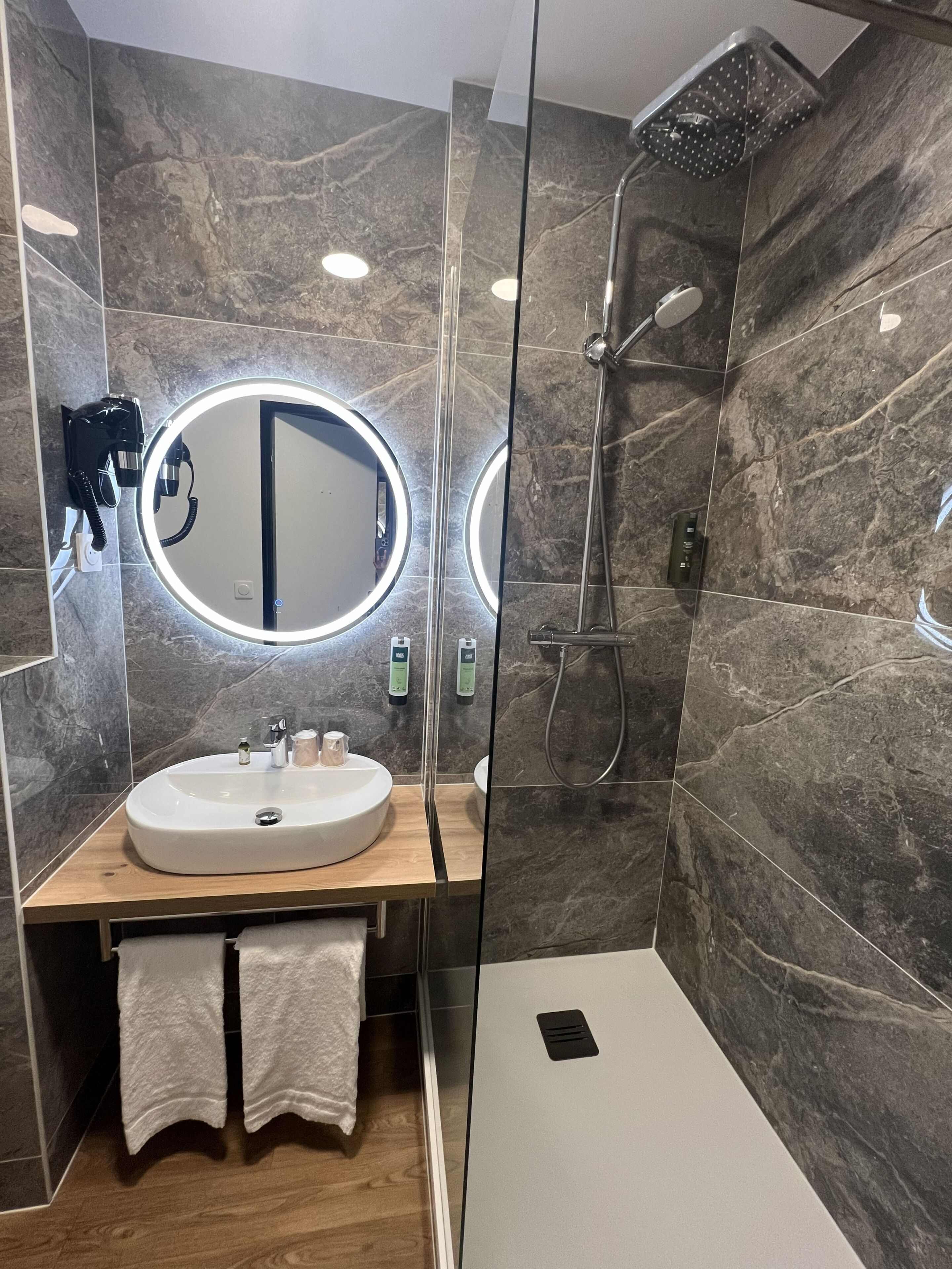 Une salle de bain moderne avec un grand miroir, un lavabo, une douche et des toilettes.