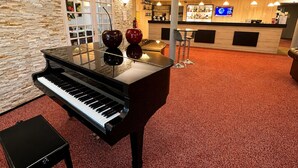 Um piano de cauda imponente num hall com parede de pedra, balcão de recepção e área de bar.