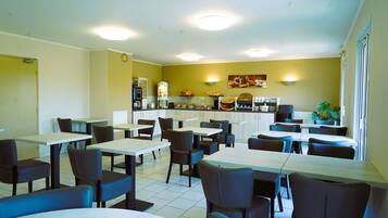 A restaurant with tables and chairs, a counter with a coffee machine, and a wall with a fruit display.