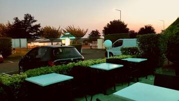 An outdoor seating area with tables and chairs, a car, and a building in the background.