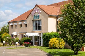 A hotel with a reception area, a parking lot, and well-maintained landscaping. - Hôtel Altina (Pacy-sur-Eure)