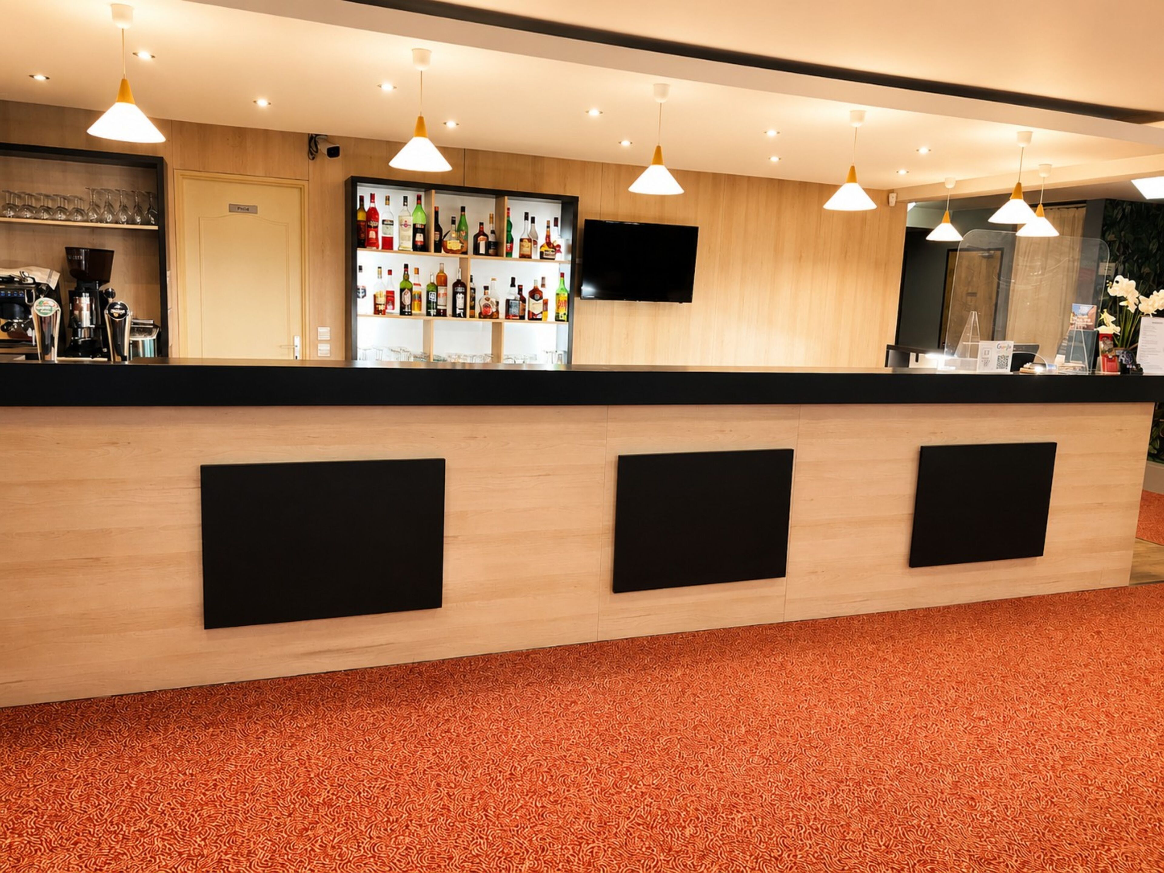 A bar area with a wooden counter, shelves with bottles, a flat-screen TV, and pendant lights.