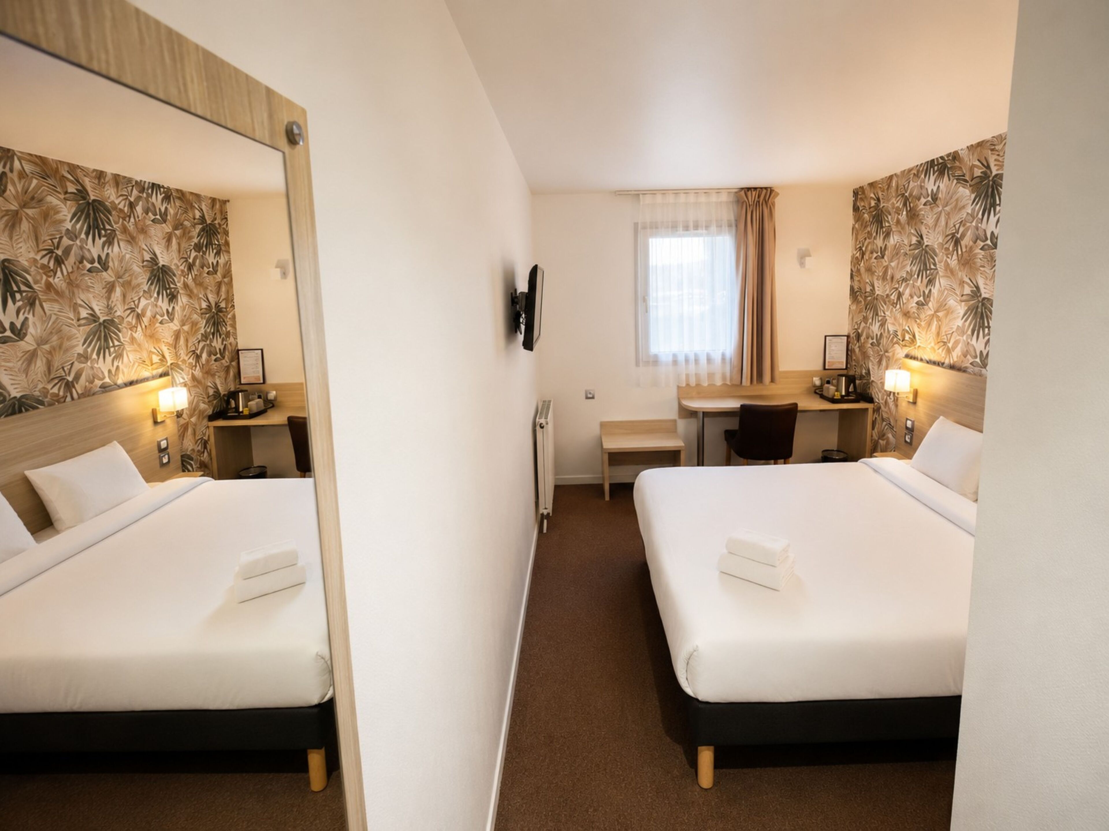 Une chambre d’hôtel avec deux lits, un bureau, une chaise, un miroir et une fenêtre avec des rideaux.