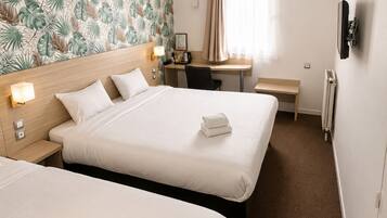 Ein Hotelzimmer mit zwei Betten, einem Schreibtisch, einem Stuhl, einem kleinen Tisch, einem Heizkörper und einer Wand mit einem tropischen Blattmuster.