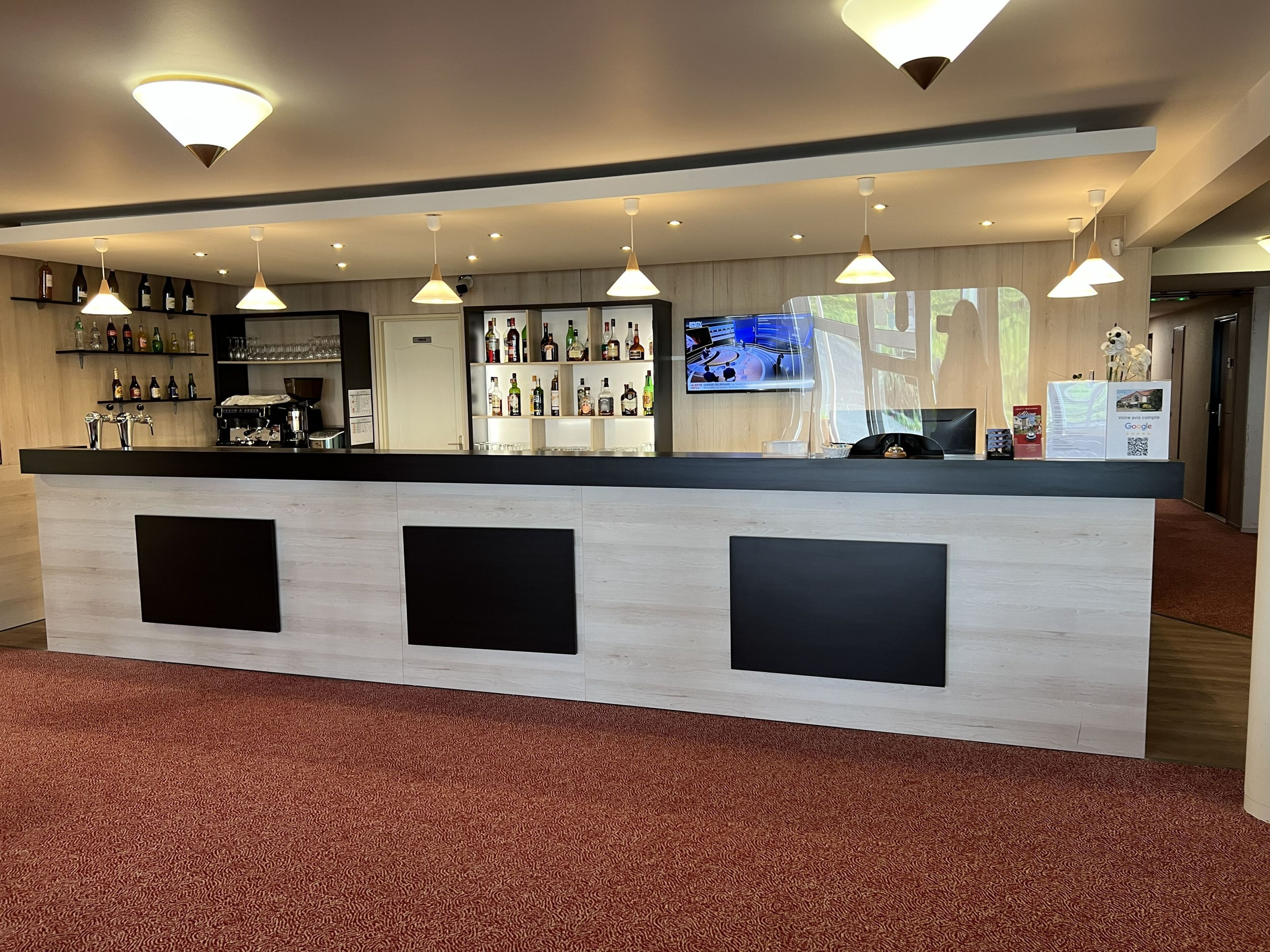 A reception desk with a flat-screen TV, multiple shelves of liquor bottles, and a coffee machine.