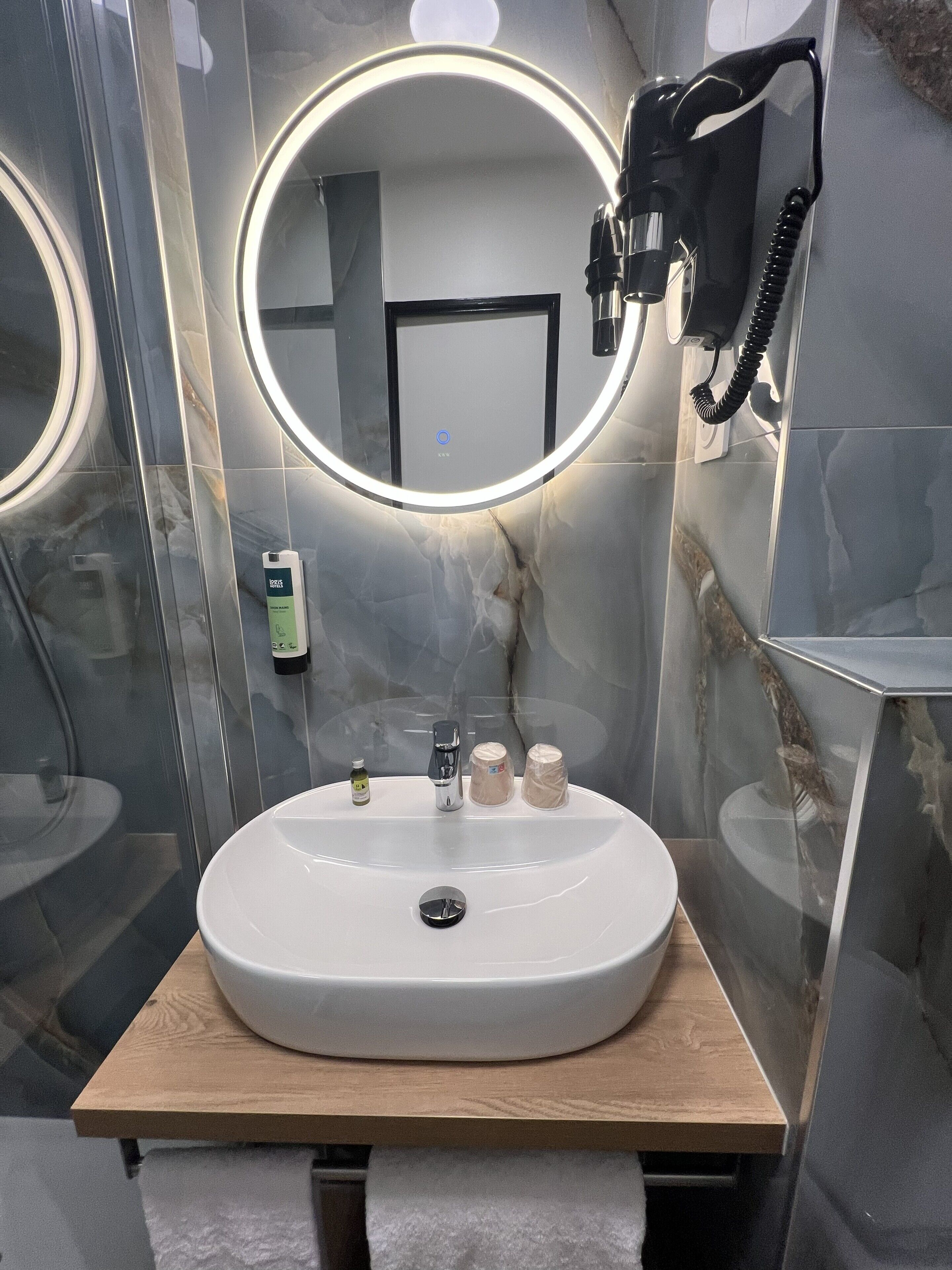 Un baño moderno con un espejo redondo, un lavamanos y un teléfono portátil.