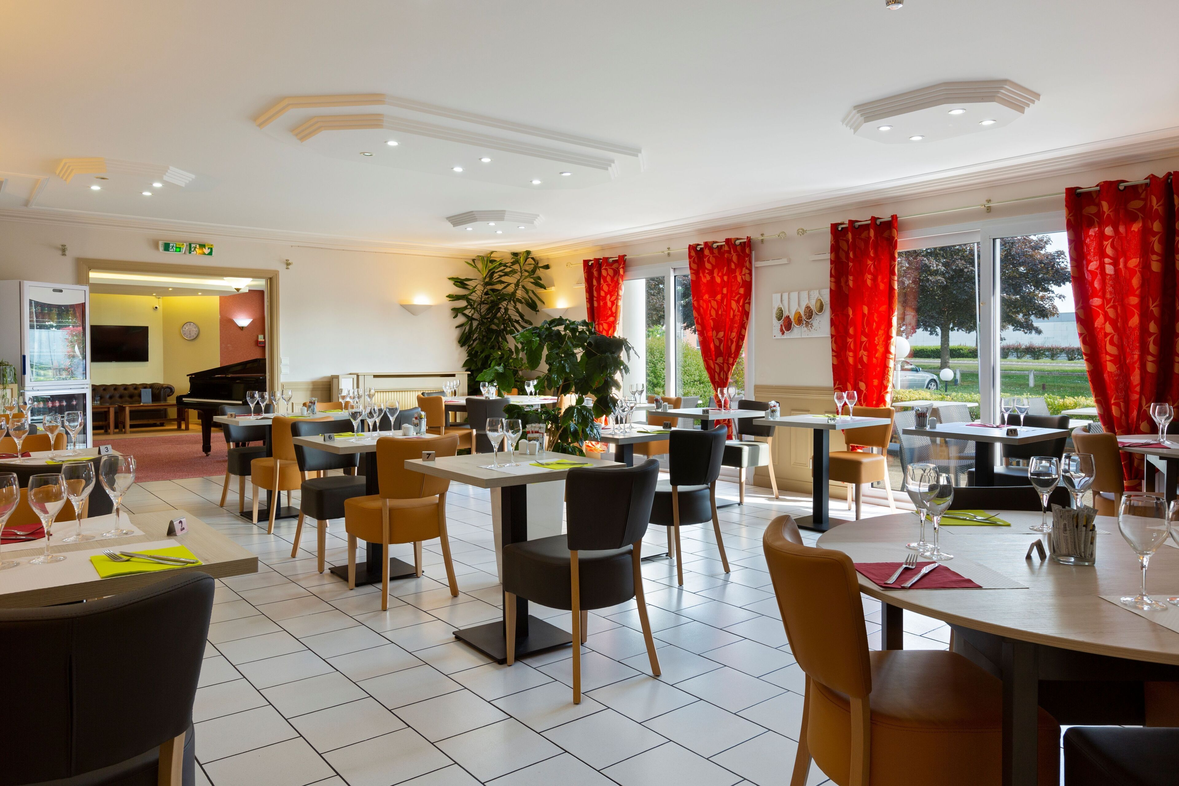 Ein Restaurant mit Tischen, Stühlen, einem Klavier und einer großen Pflanze.