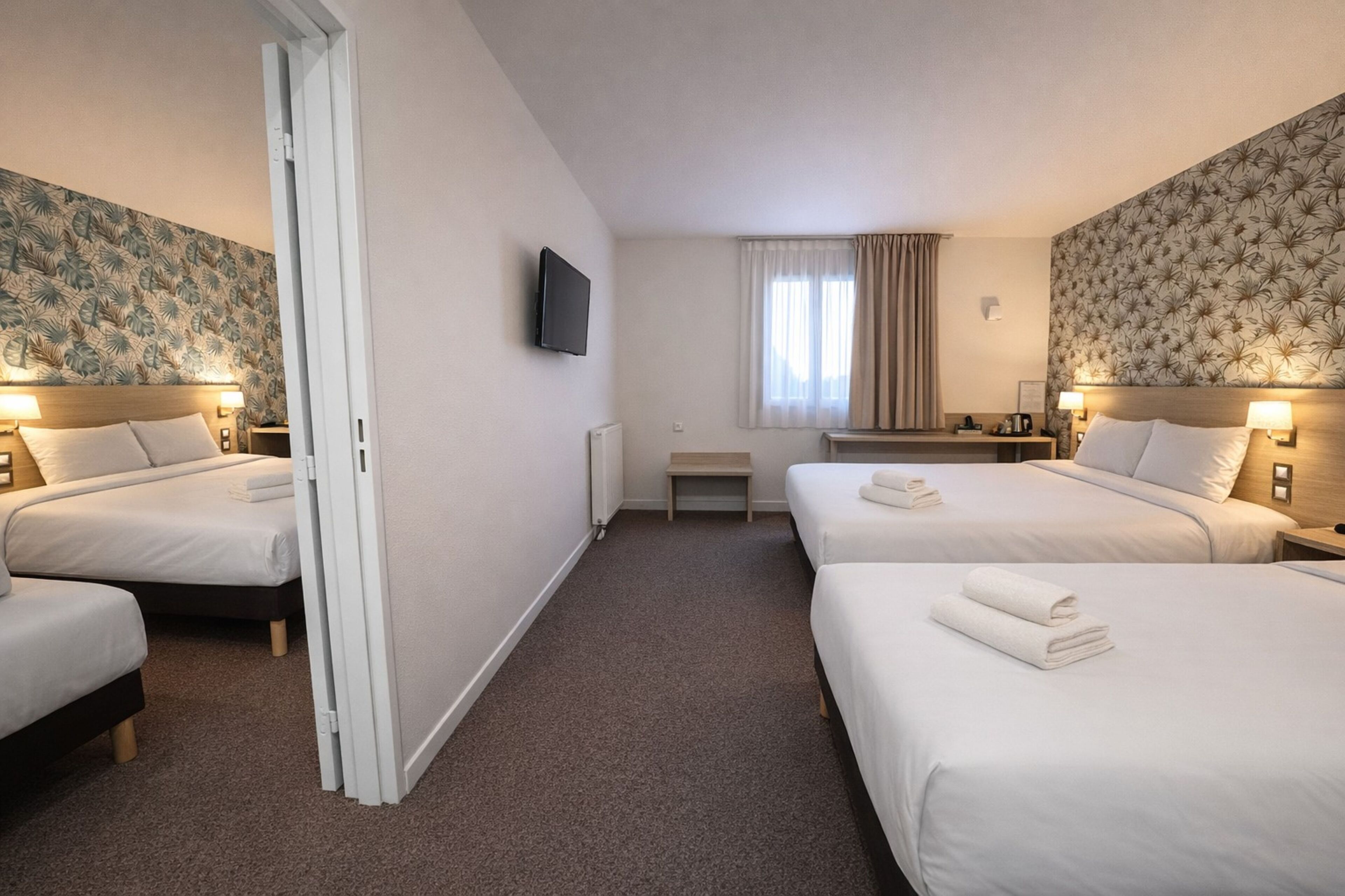 Une chambre d’hôtel avec deux lits, une télévision, un bureau et une fenêtre avec des rideaux.