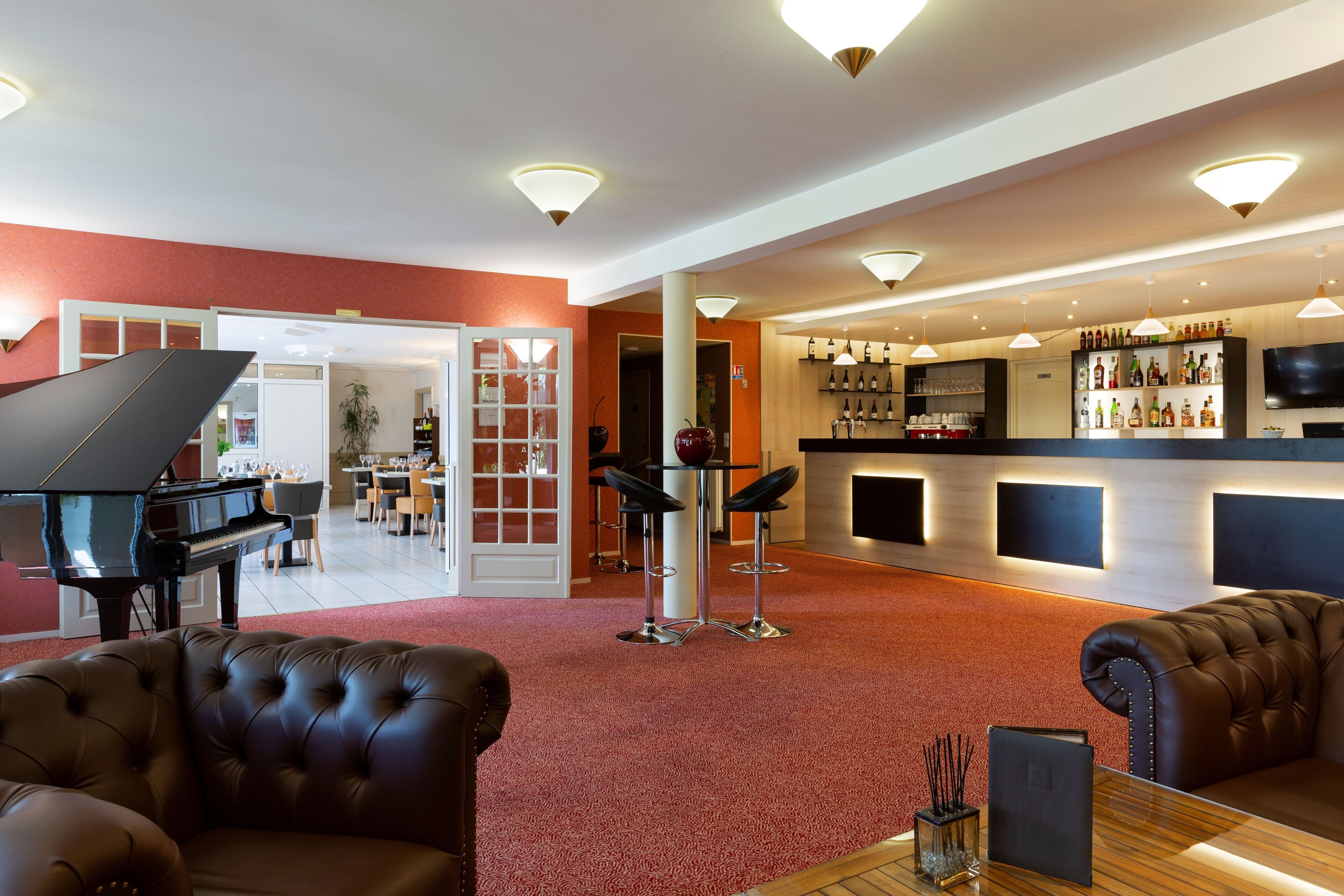 A hotel lobby with a grand piano, leather sofas, a bar area with a variety of liquor bottles, and a television mounted on the wall.