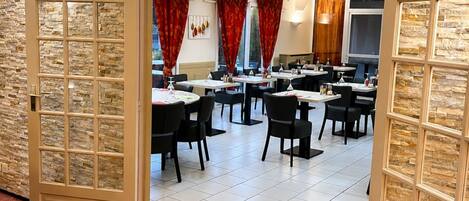 Una habitación de hotel con pared de piedra, alfombra roja estampada y un comedor con mesas y sillas.
