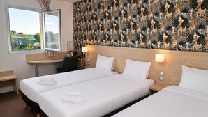 Quarto de hotel com duas camas, uma escrivaninha, uma cadeira e vista para o exterior.