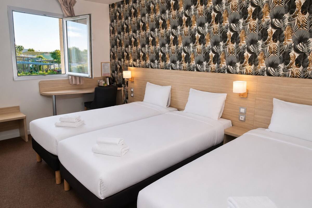 Habitación de hotel con dos camas, un escritorio, una silla y vistas al exterior.
