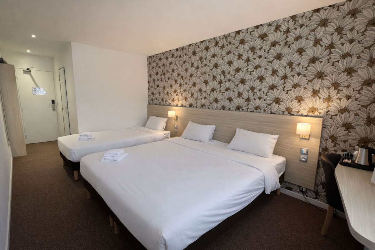Habitación de hotel con dos camas, cabecera de madera, papel tapiz floral y un escritorio con silla.