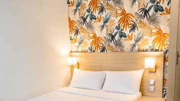 A hotel room with a bed, two bedside lamps, a nightstand, and a wall with a tropical leaf pattern.