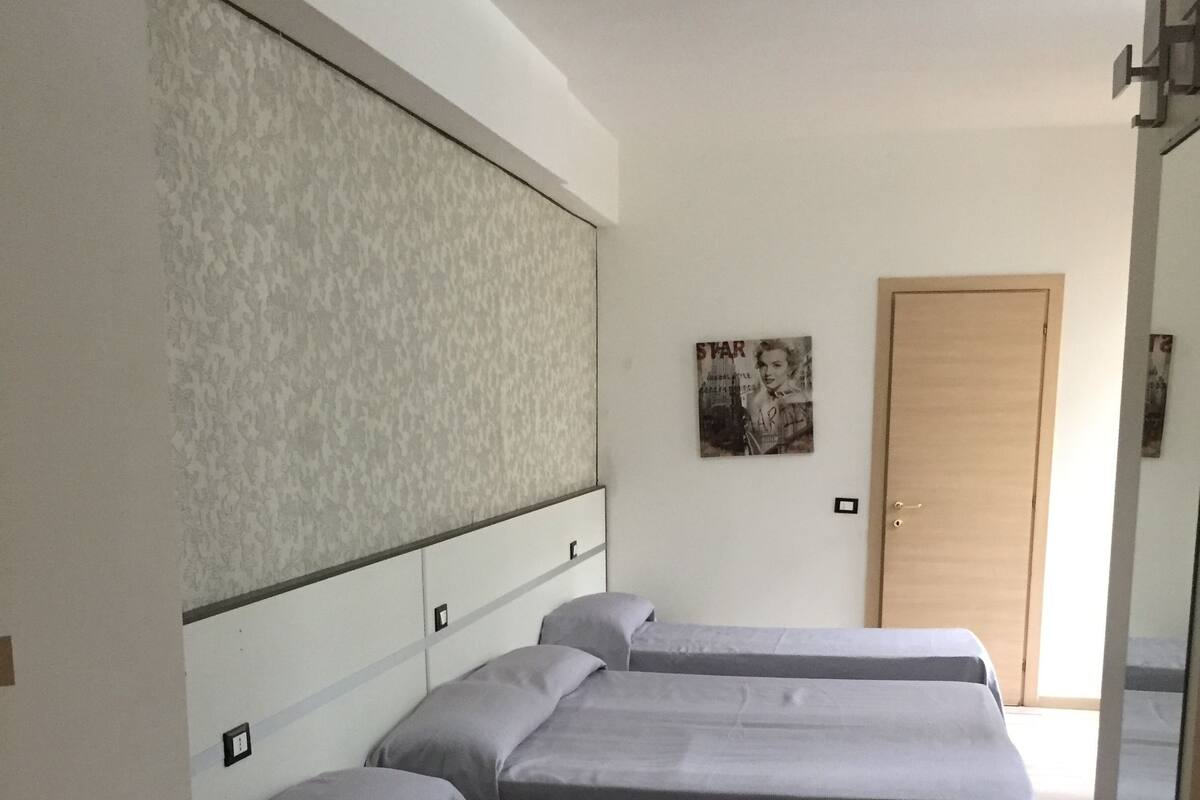 A hotel room with three single beds, a large wall unit, a door, and a poster on the wall.