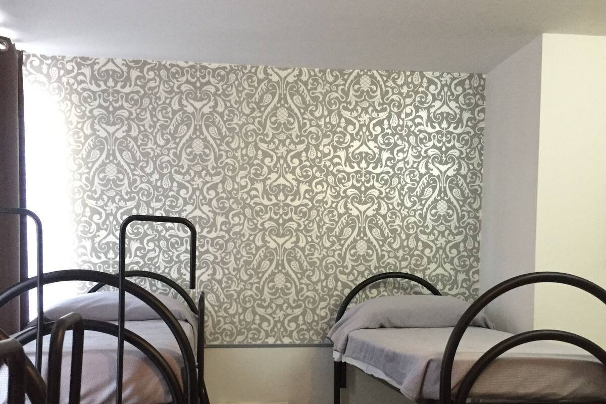 A dormitory room with bunk beds, a small bedside table, and patterned wallpaper.