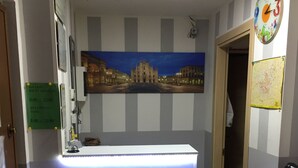 A reception desk with a cityscape painting above it, a clock, and a map on the wall. - Scacco Matto (Milan)