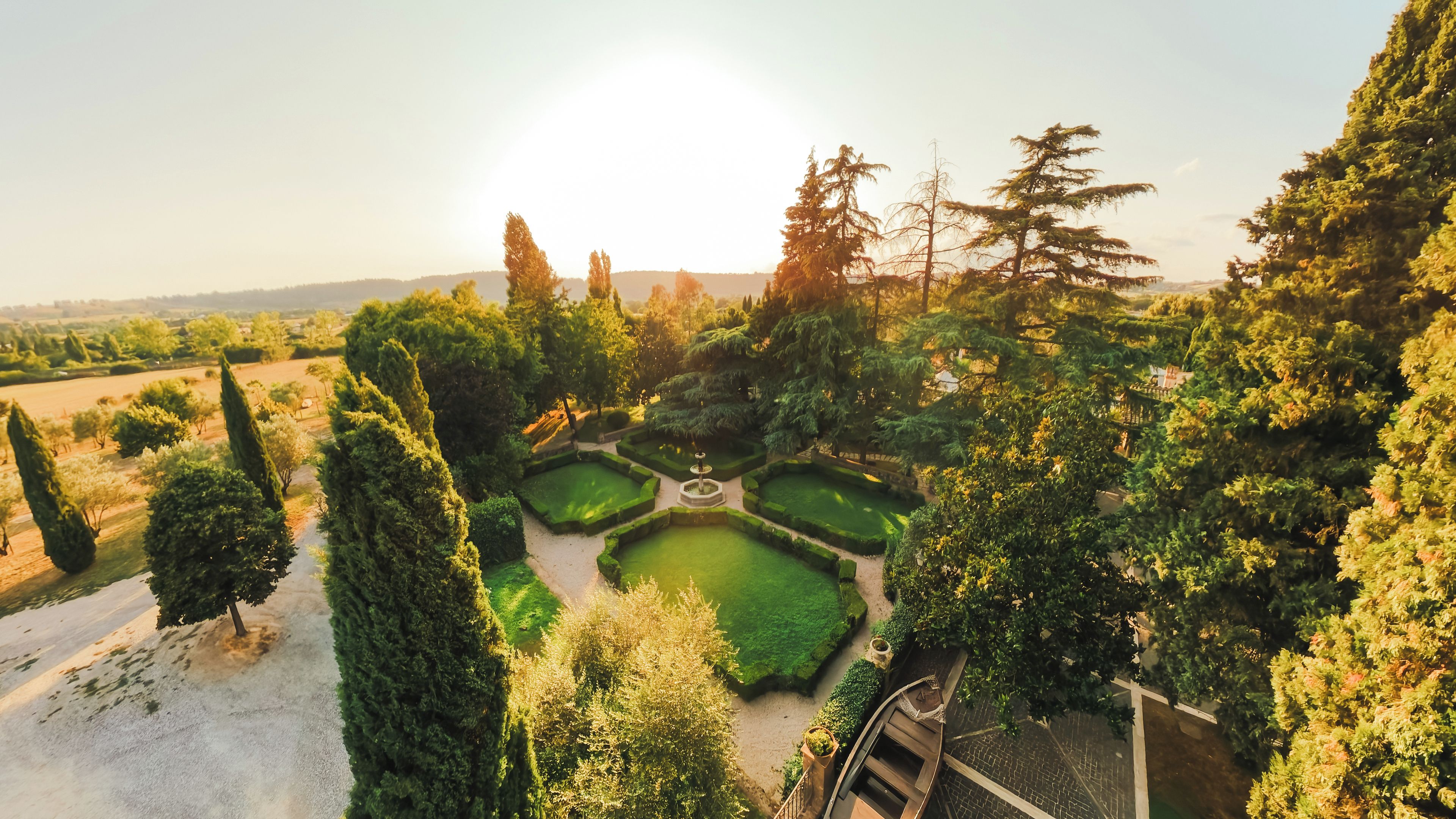 A formal garden with geometric hedges, a central fountain, and a variety of trees.