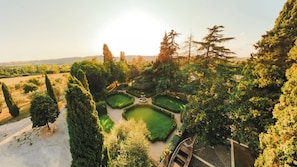 A formal garden with geometric hedges, a central fountain, and a variety of trees.