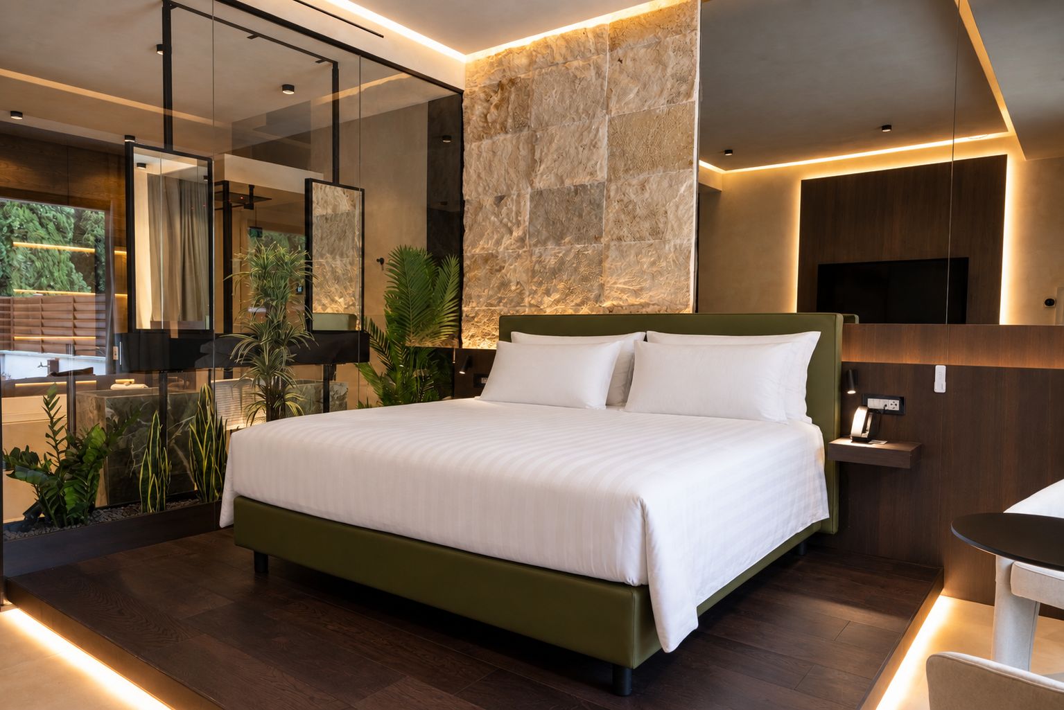 Een moderne slaapkamer met een groot bed, een glazen scheidingswand en een accentmuur van steen.