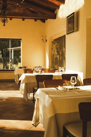 Een restaurant met gedekte tafels, een groot schilderij aan de muur en een kroonluchter.