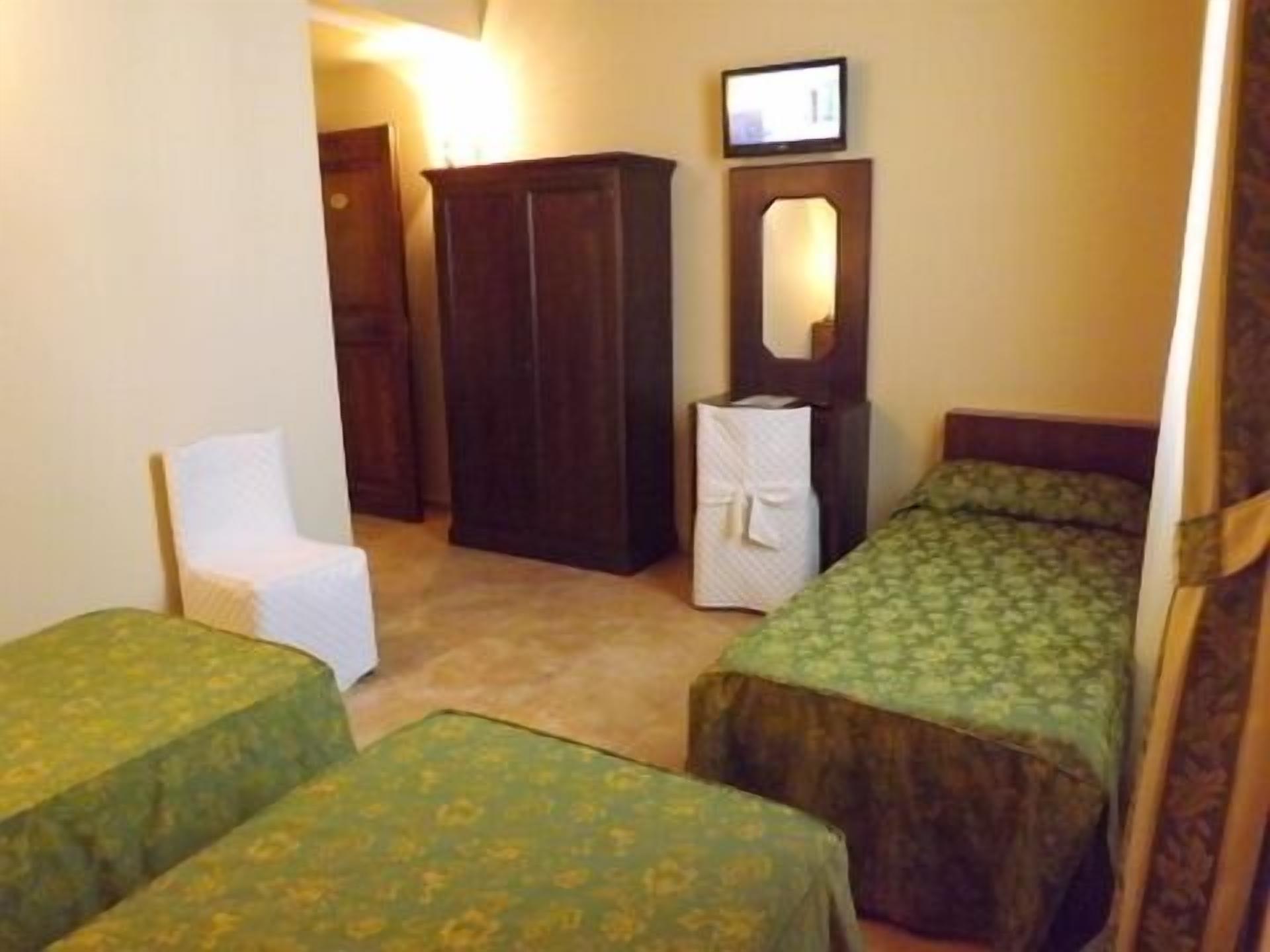 A small room with two single beds, a chair, a wardrobe, and a mirror.