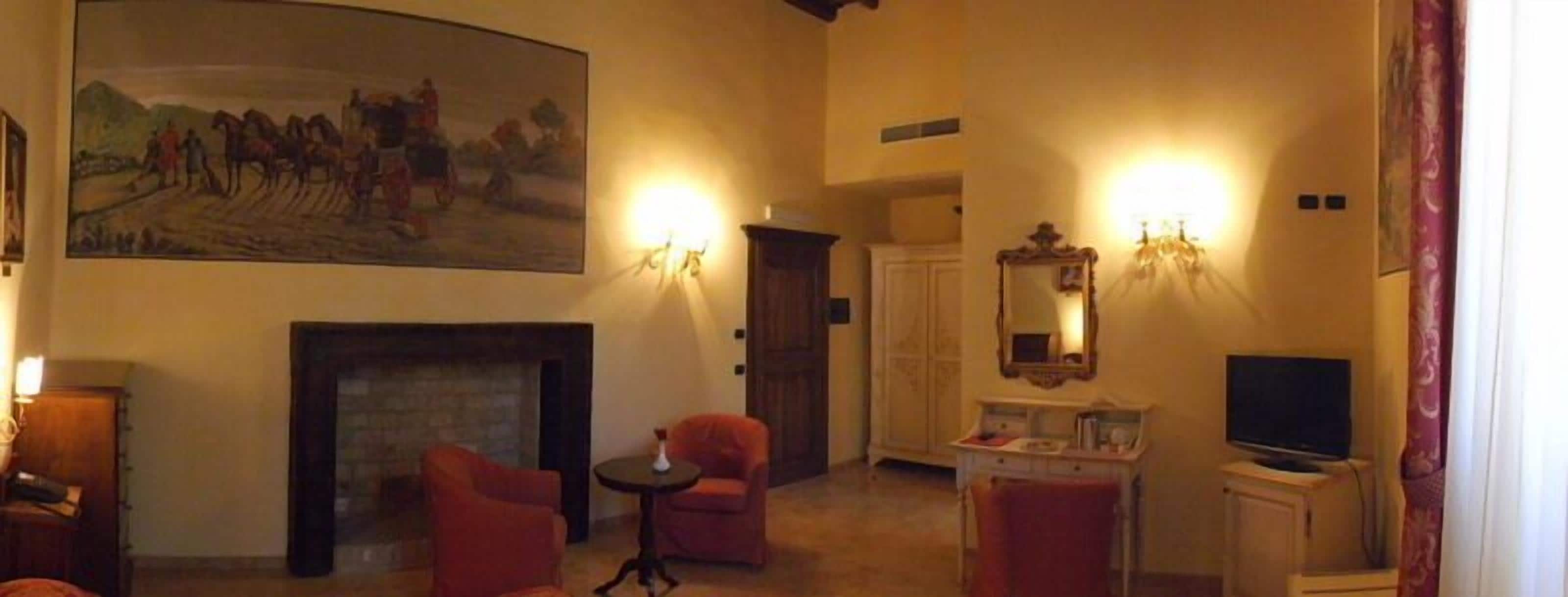 A room with a fireplace, two armchairs, a small table, a television, and a painting on the wall.