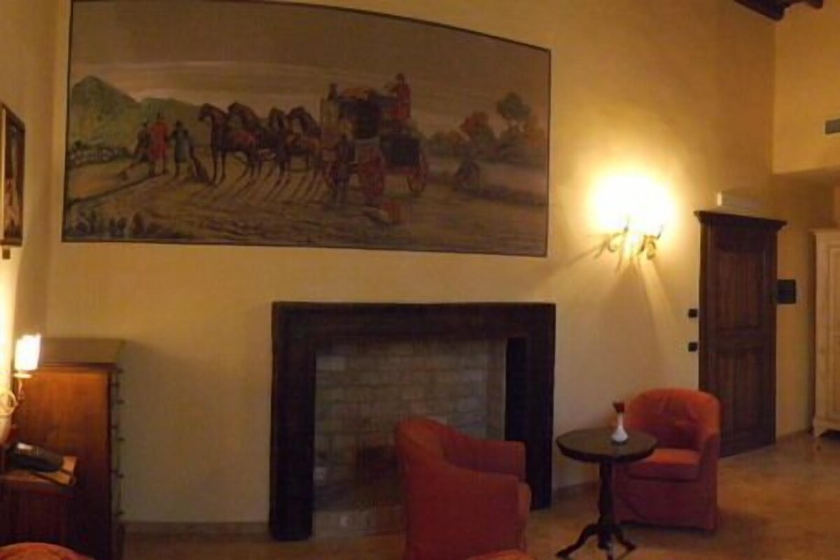 Une pièce avec une cheminée, deux fauteuils, une petite table, un téléviseur et un tableau au mur.