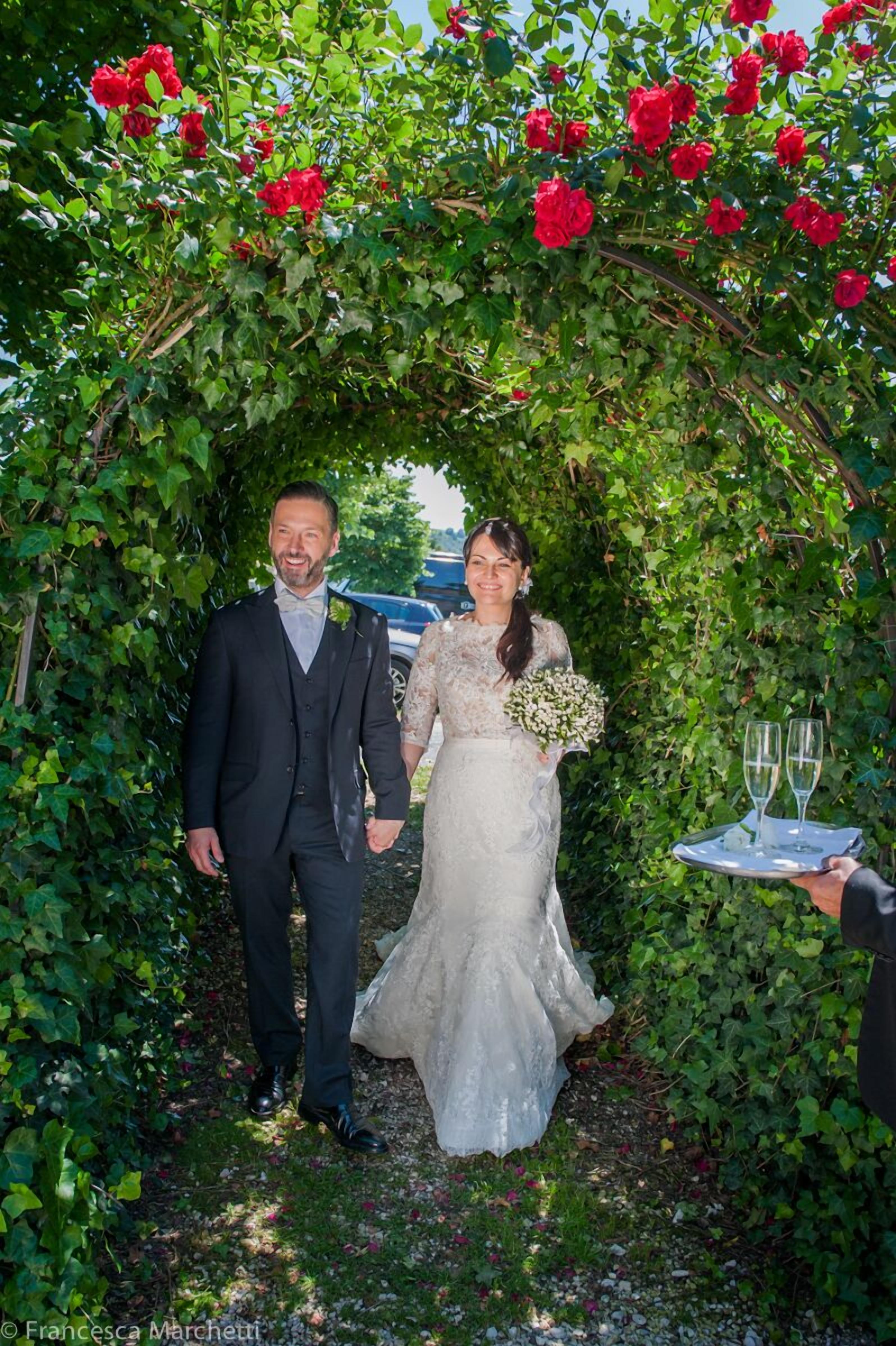 A couple walking through a garden archway with red roses.