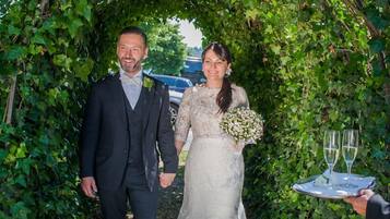 A couple walking through a garden archway with red roses.