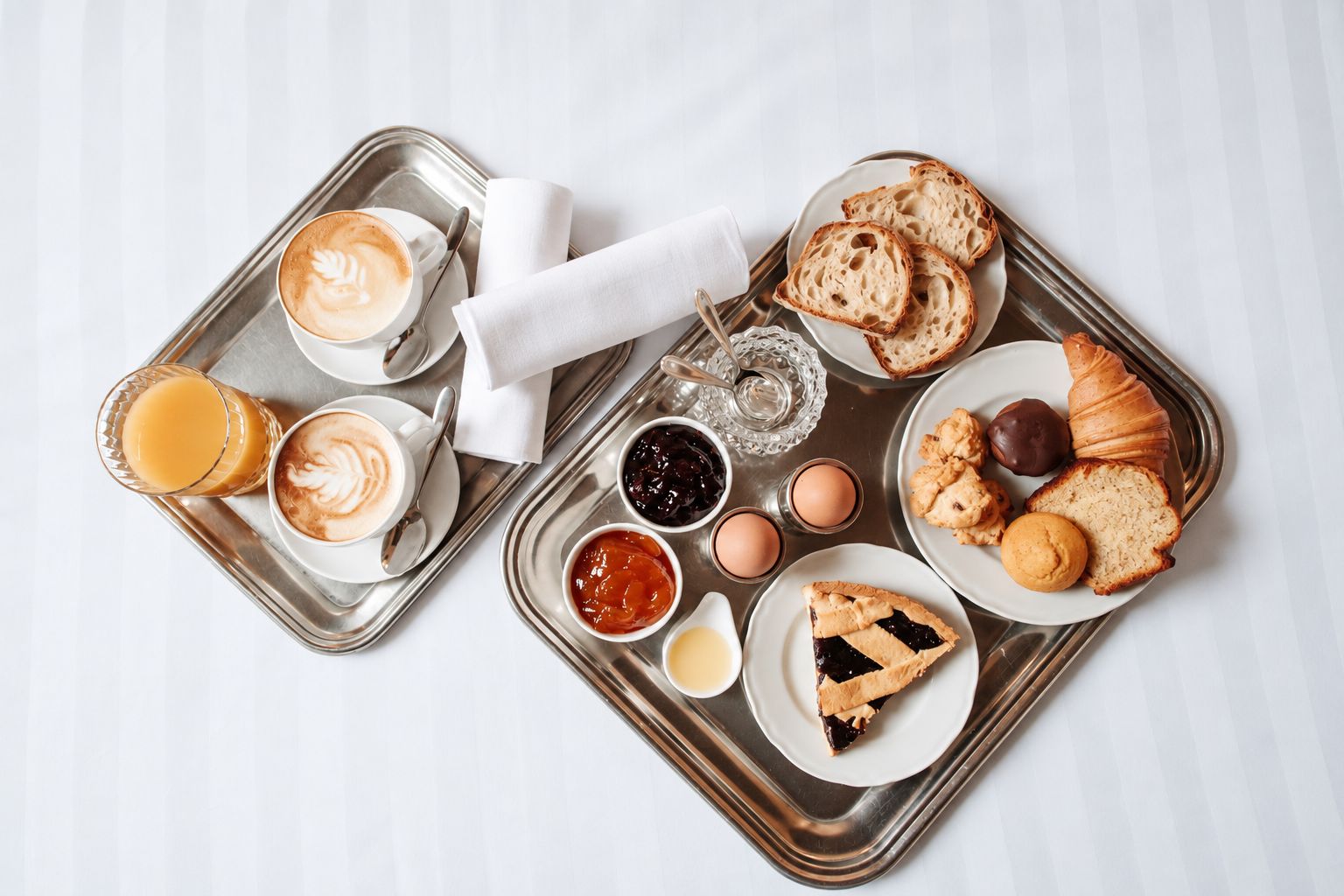 Una bandeja de desayuno con café, croissants, pastelería, mermelada y huevos.