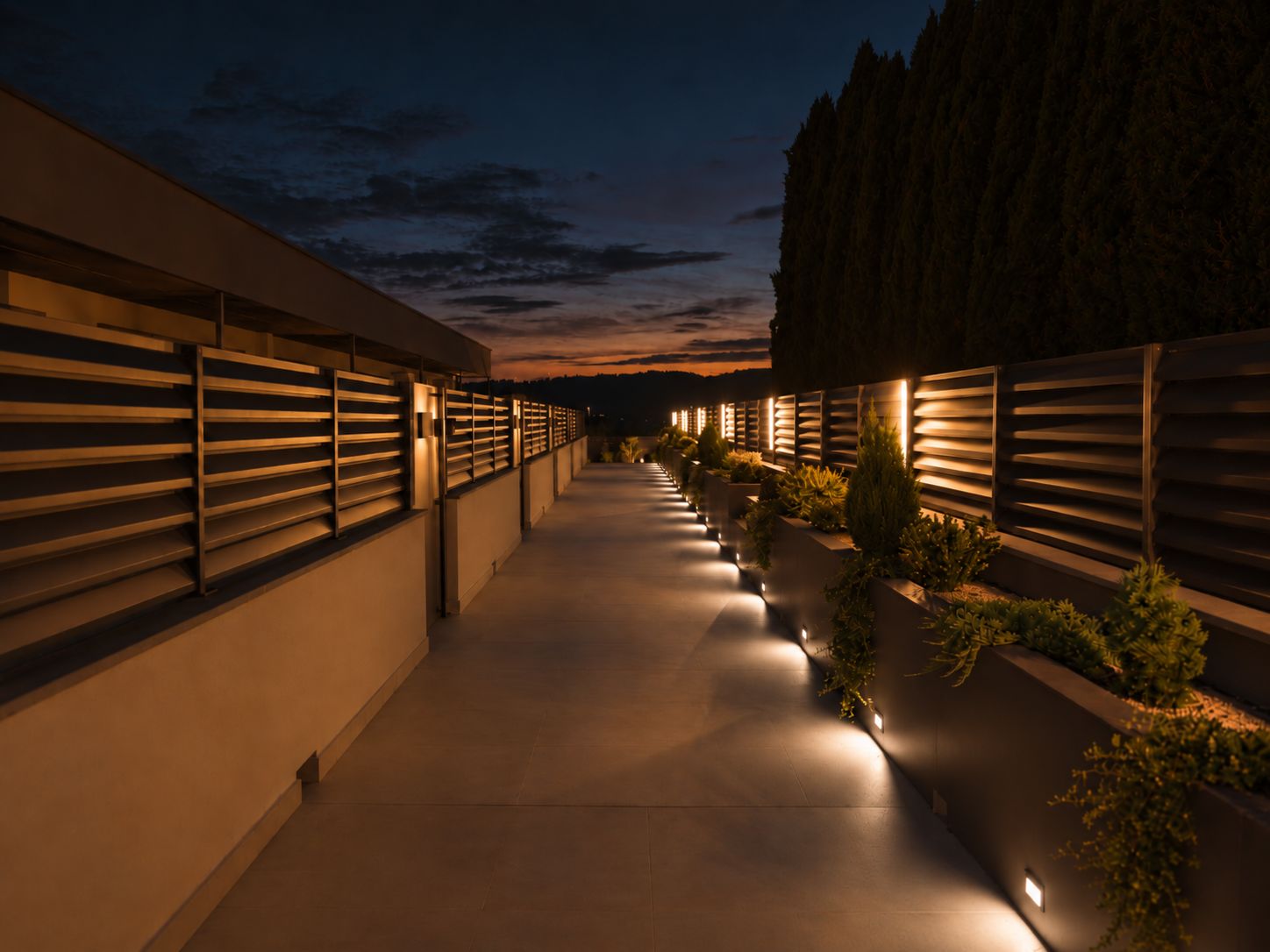 Un sendero bordeado por edificios modernos con listones verticales iluminados, que se extiende hasta un horizonte lejano.