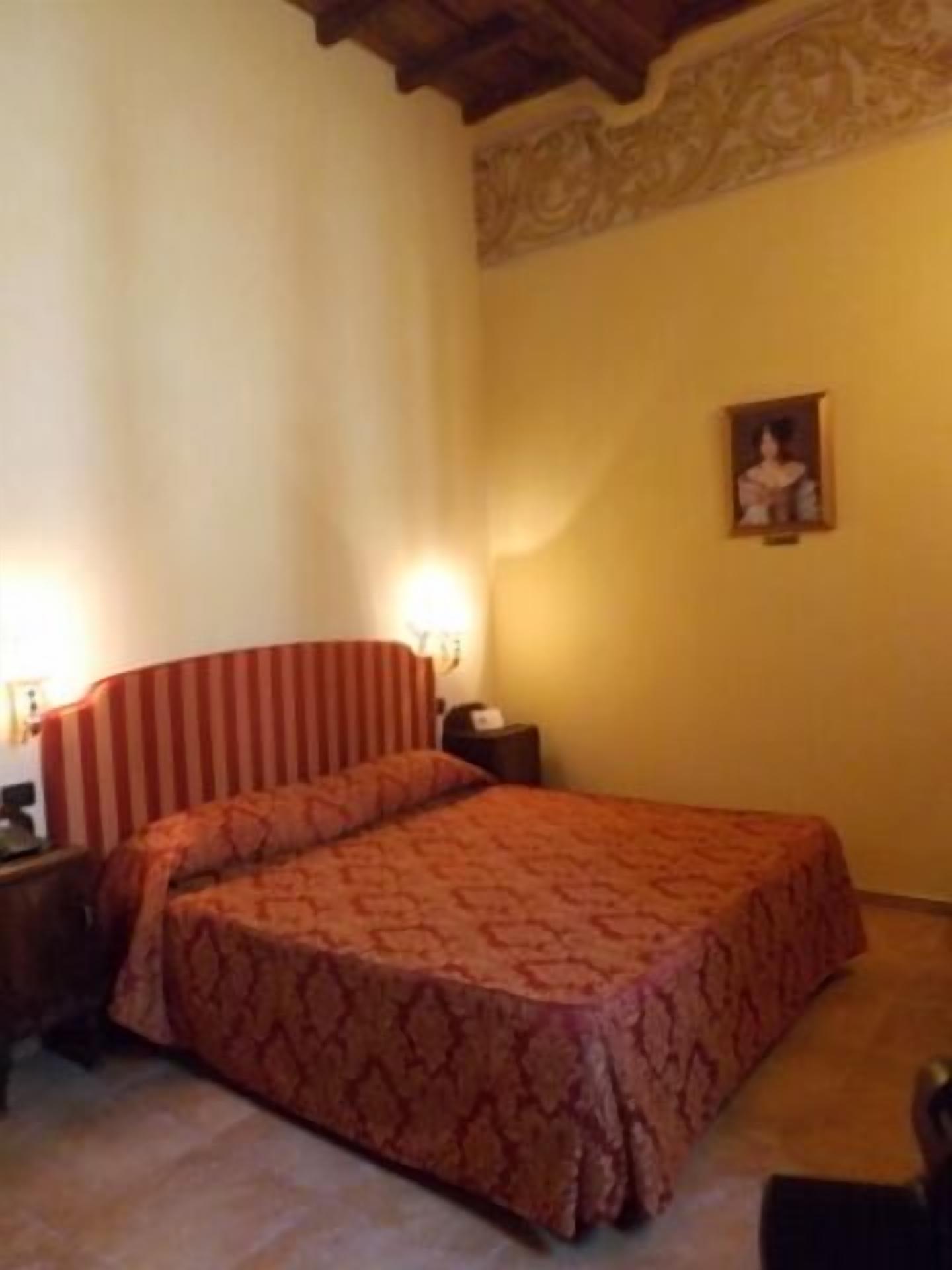 A bedroom with a bed, a nightstand, a lamp, and a wall-mounted picture.