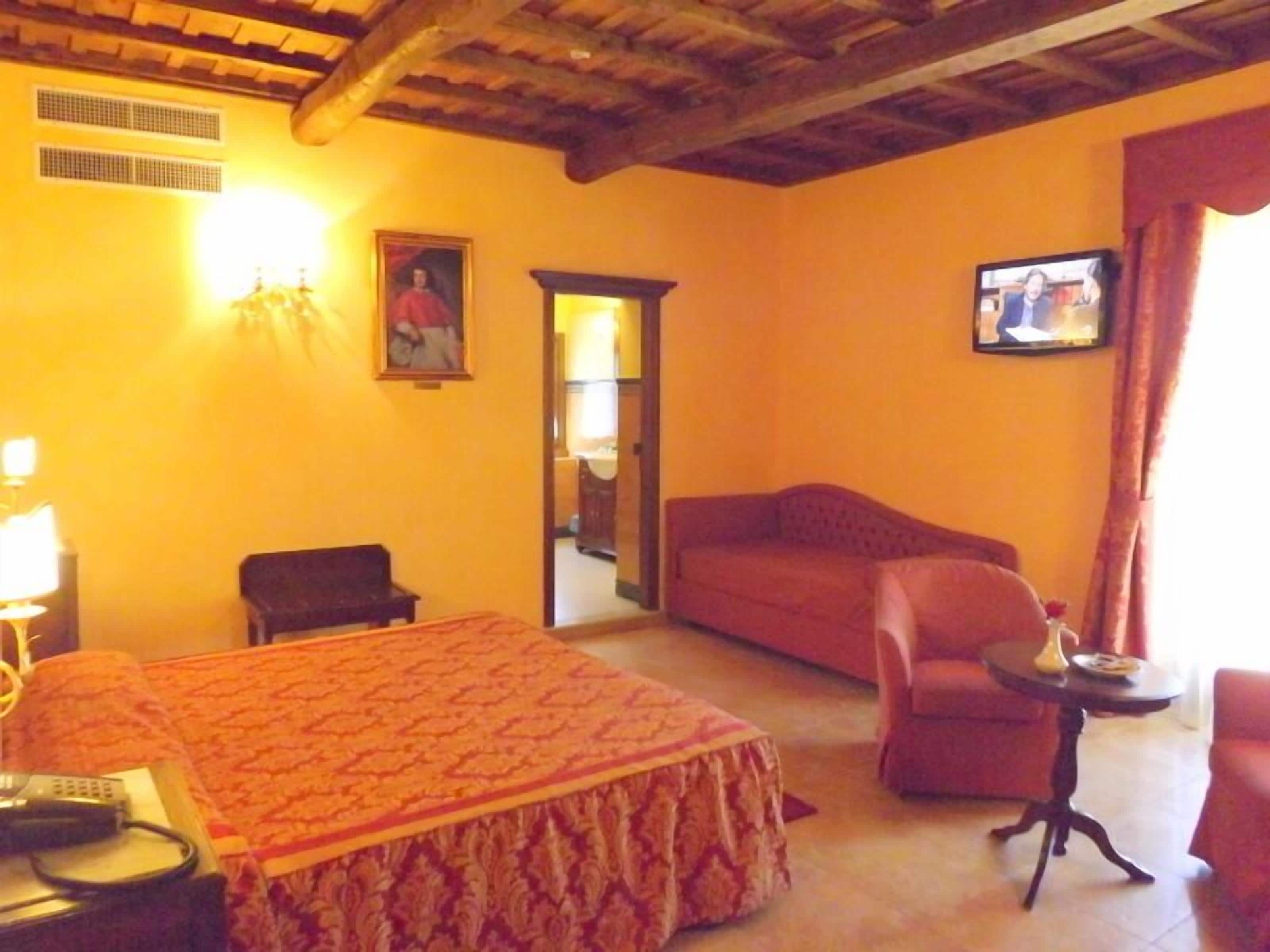 Habitación de hotel con cama, sofá, una mesita, televisor y una silla.