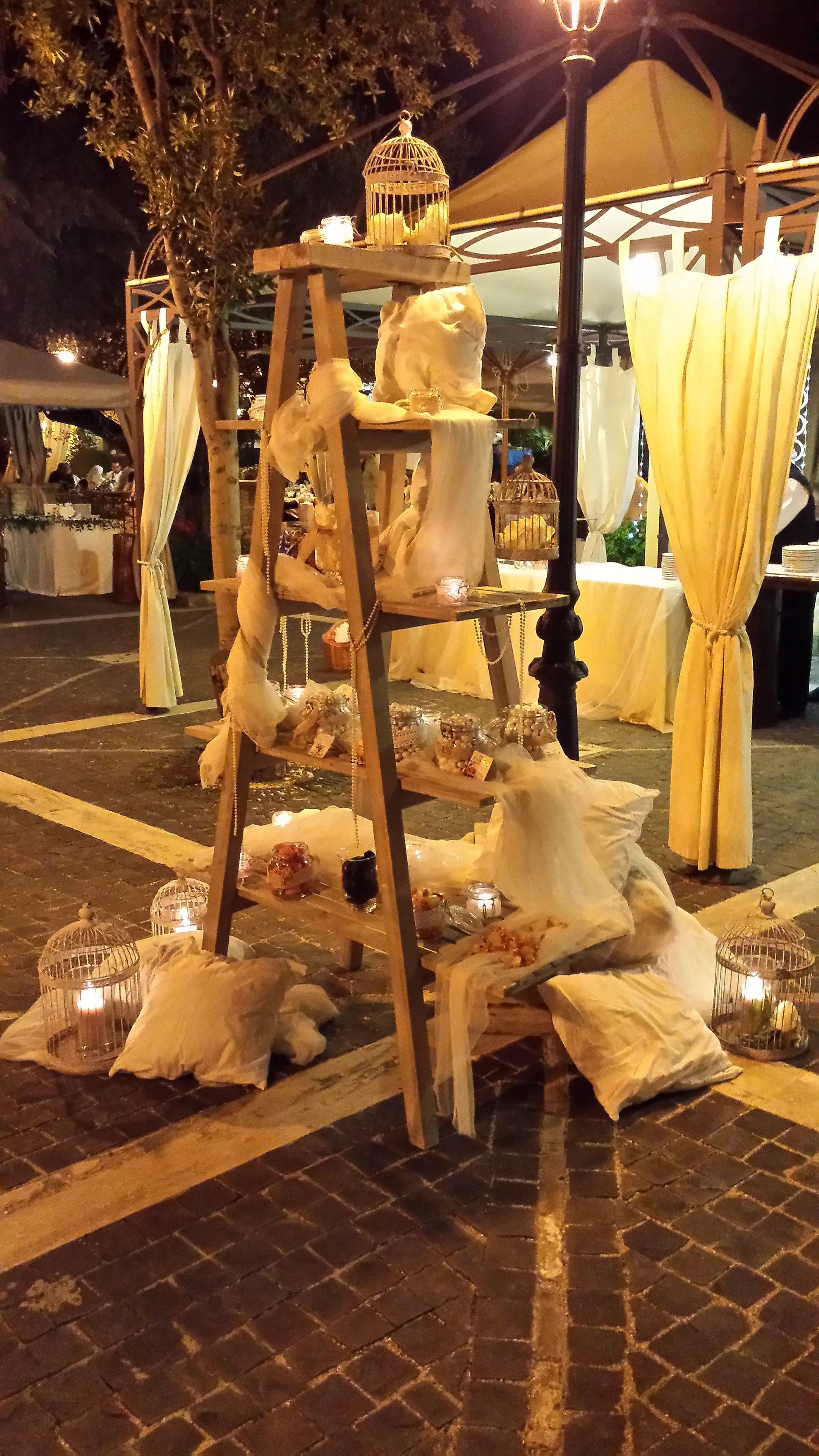 A tiered display stand with various items, possibly for a wedding or event, set up outdoors at night.