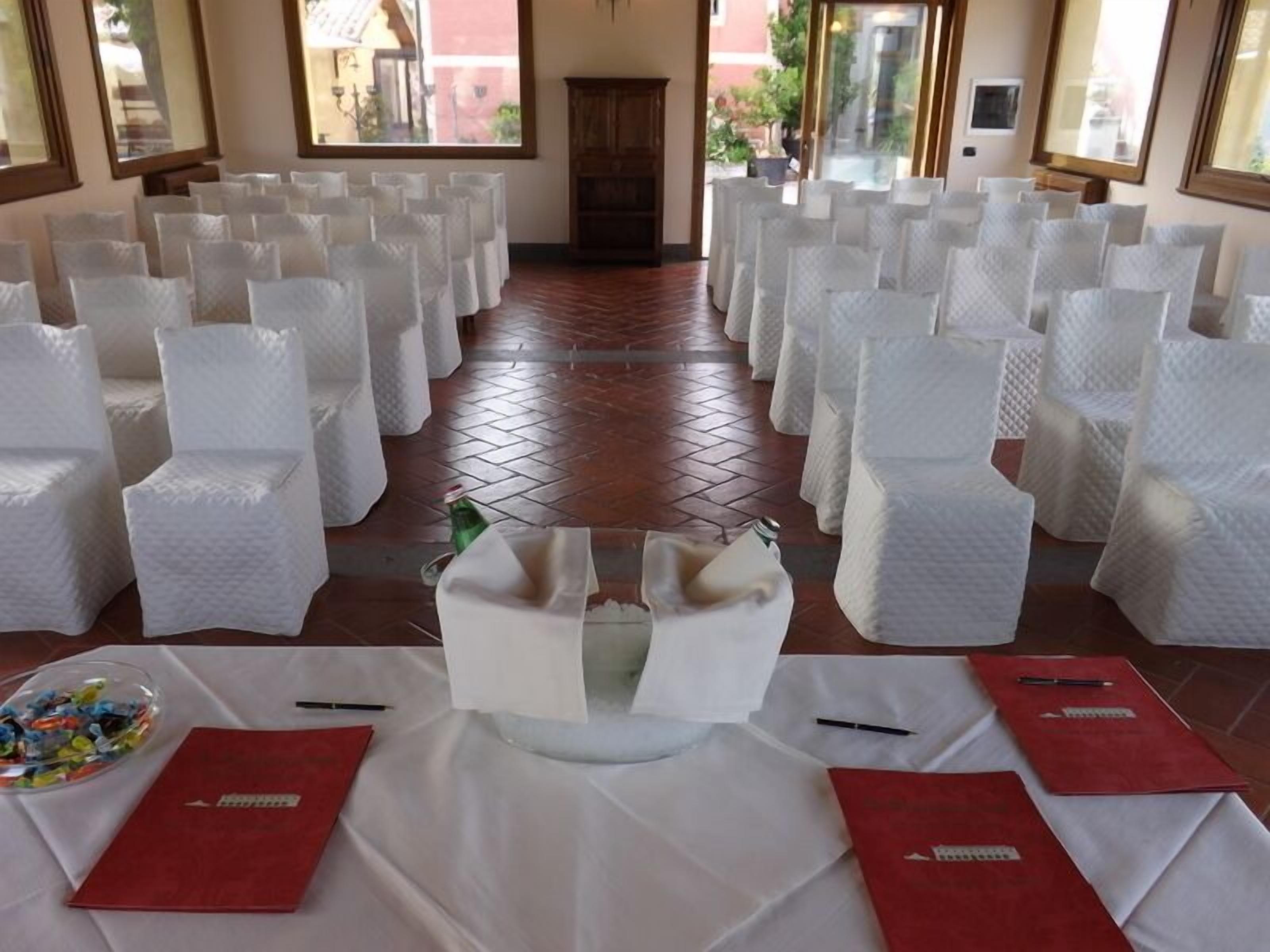 A room with rows of white chairs, a table with red folders, and a bottle on the floor.