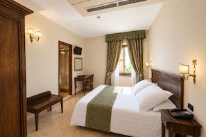 Een hotelkamer met een bed, een bureau, een stoel, een klein tafeltje, een telefoon en een raam met gordijnen.