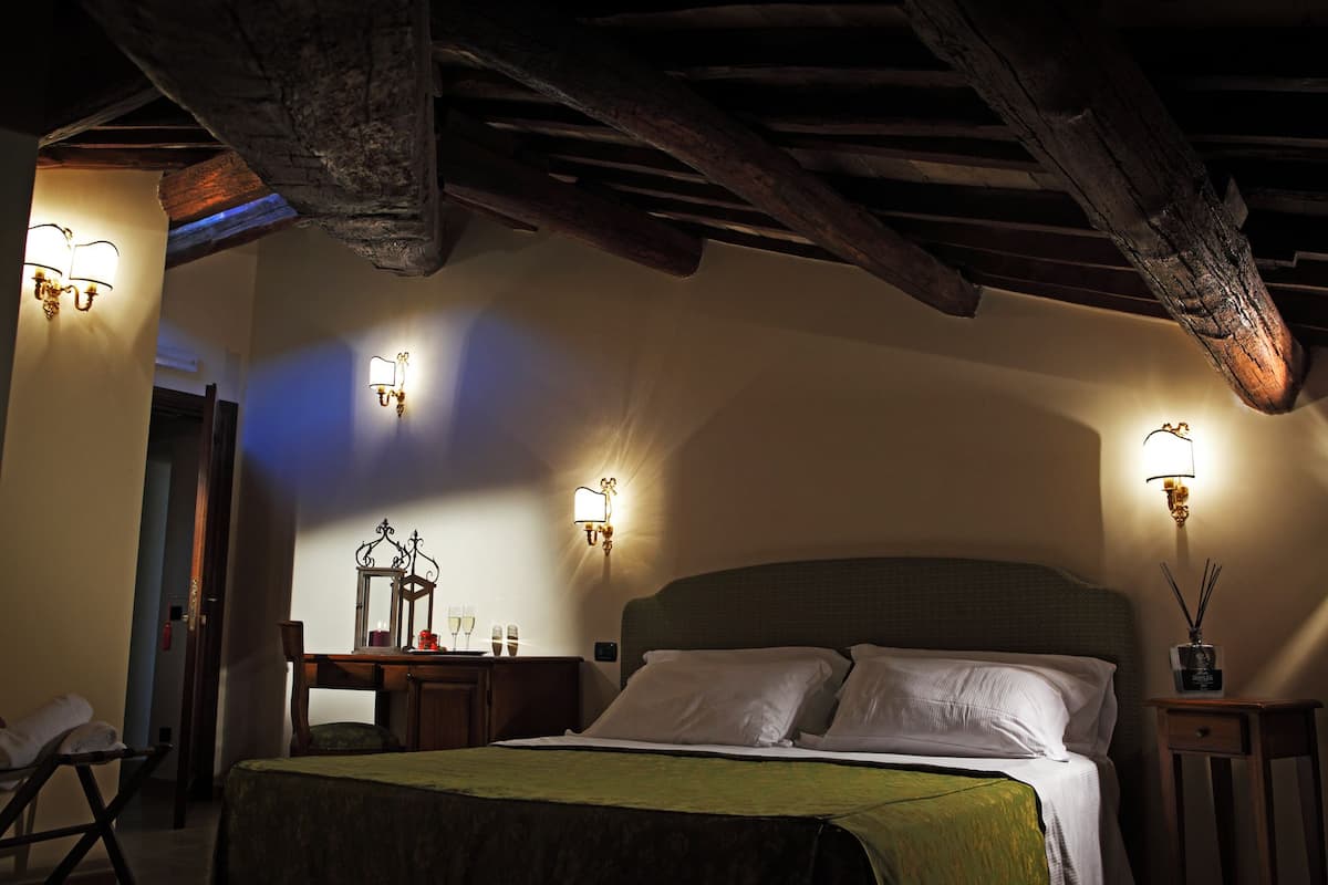 A dimly lit room with a wooden ceiling, a bed with white linens, and wall-mounted sconces.