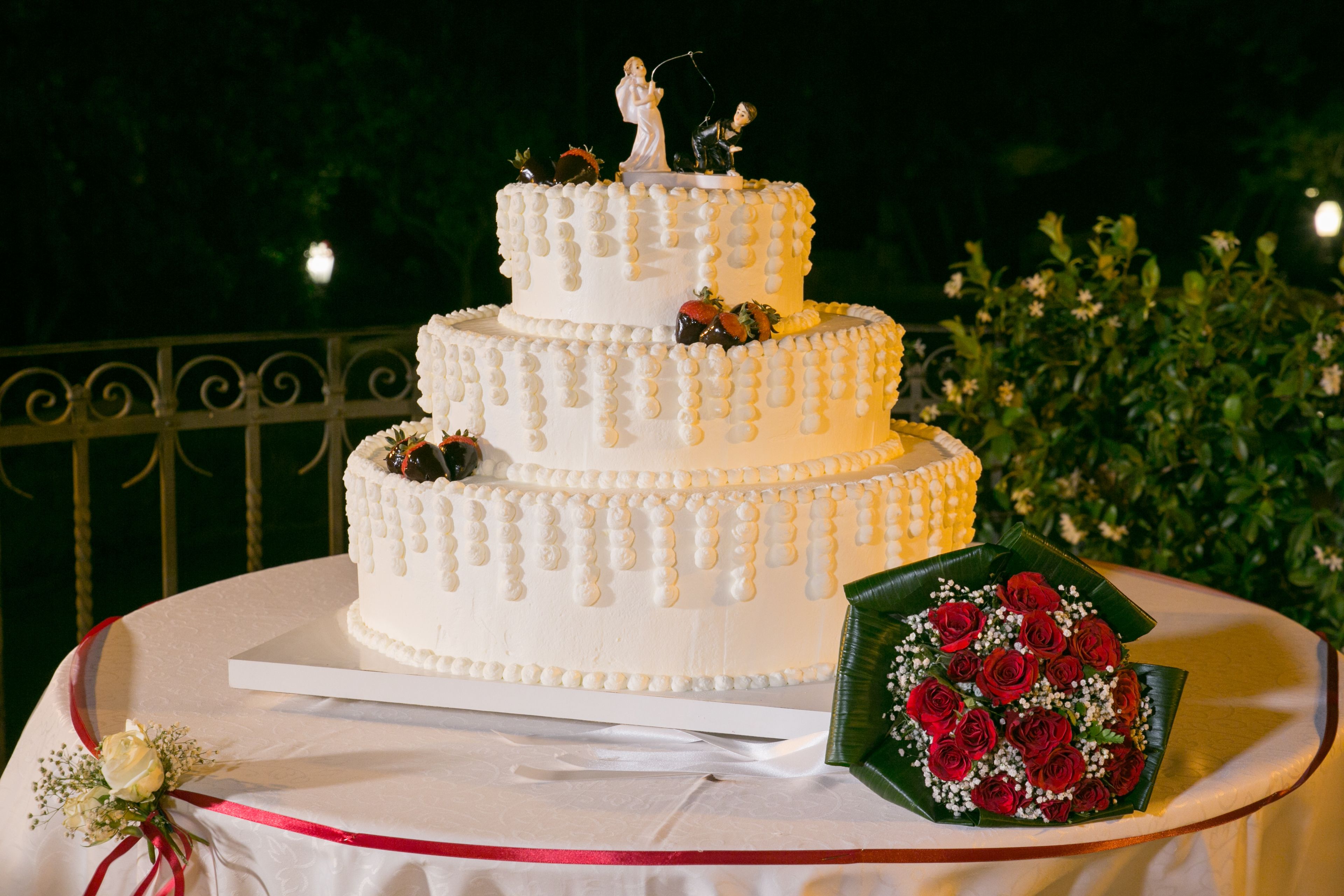 A multi-tiered white cake with a topper, placed on a round table with a white tablecloth.