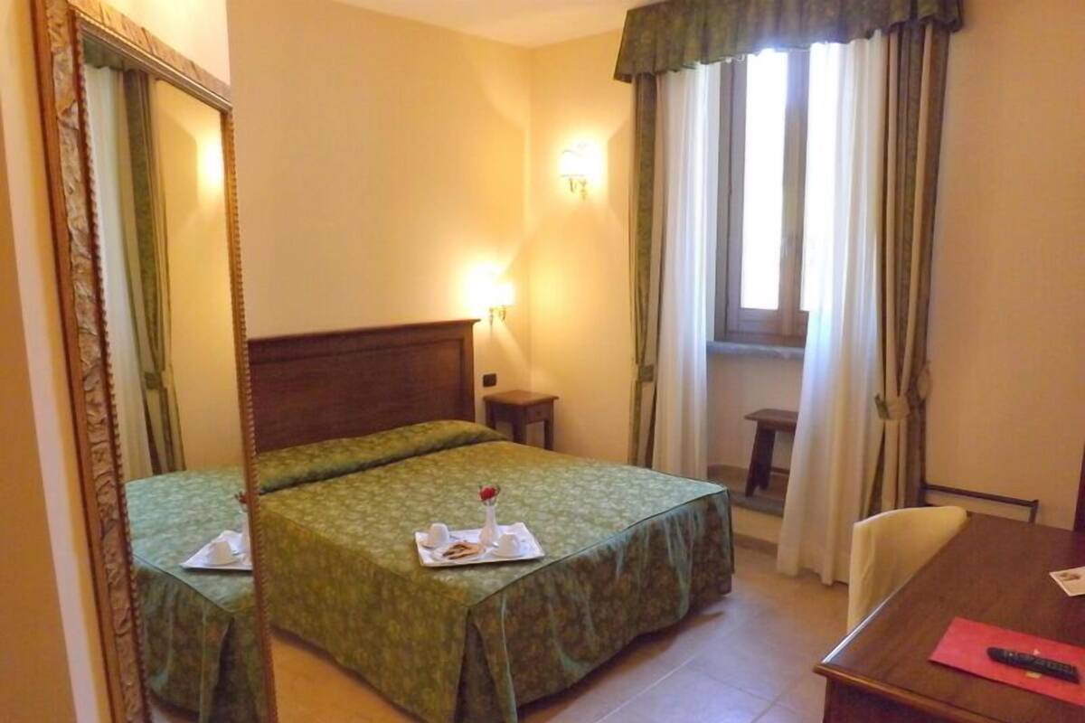 A hotel room with two beds, a desk, a chair, a lamp, and a window with curtains.