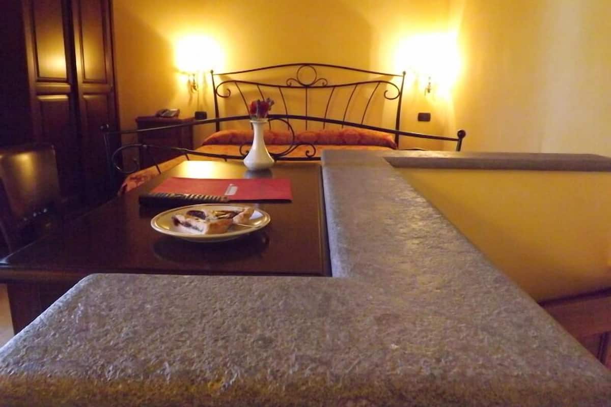 A room with a bed, a bedside table, a lamp, and a small table with a plate of food.