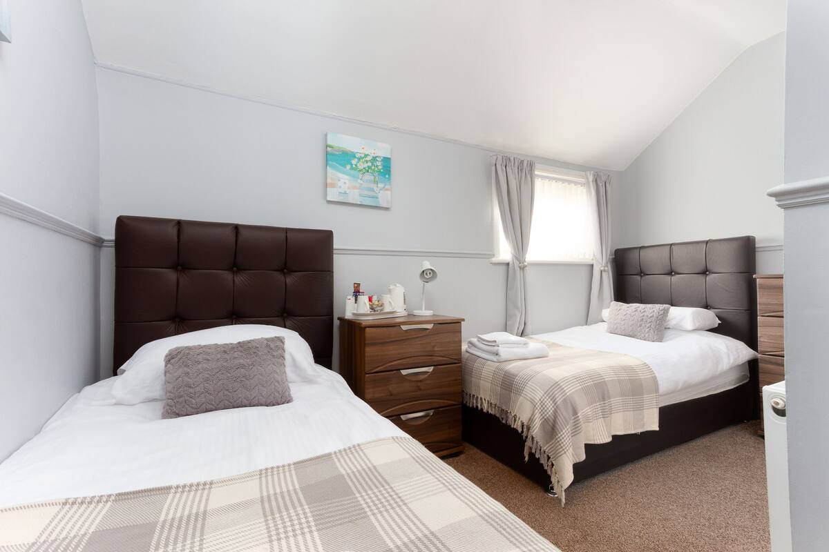A bedroom with two beds, a nightstand, a bedside table, and a painting on the wall.