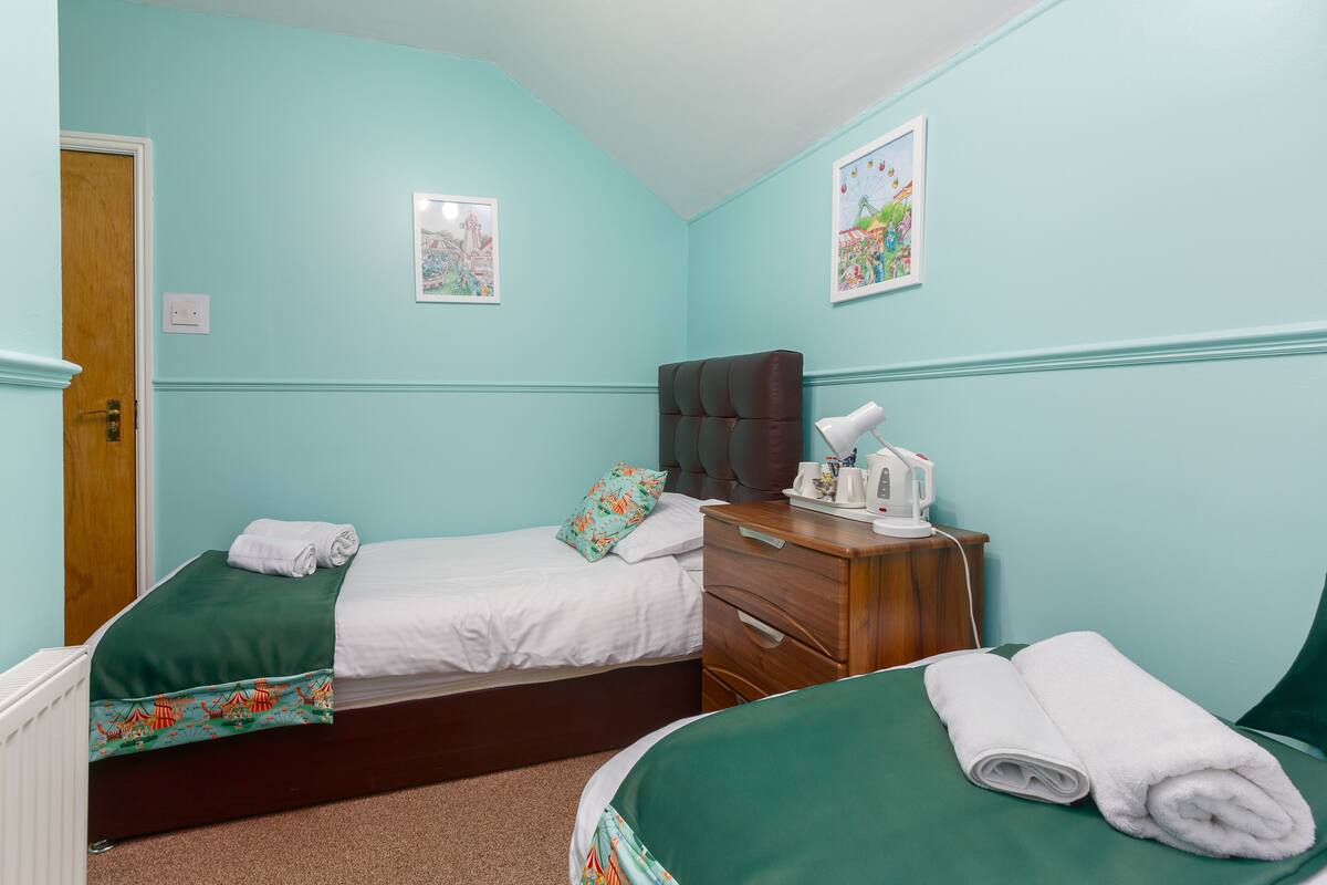 A bedroom with two beds, a wooden nightstand, and a wall-mounted lamp.