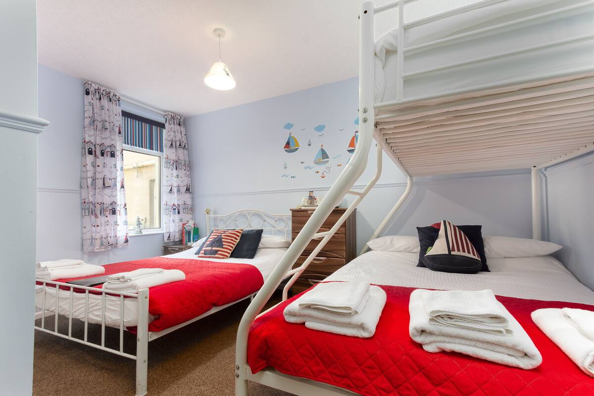 A twin room with two beds, each with a red quilt, white bedding, and neatly folded towels.