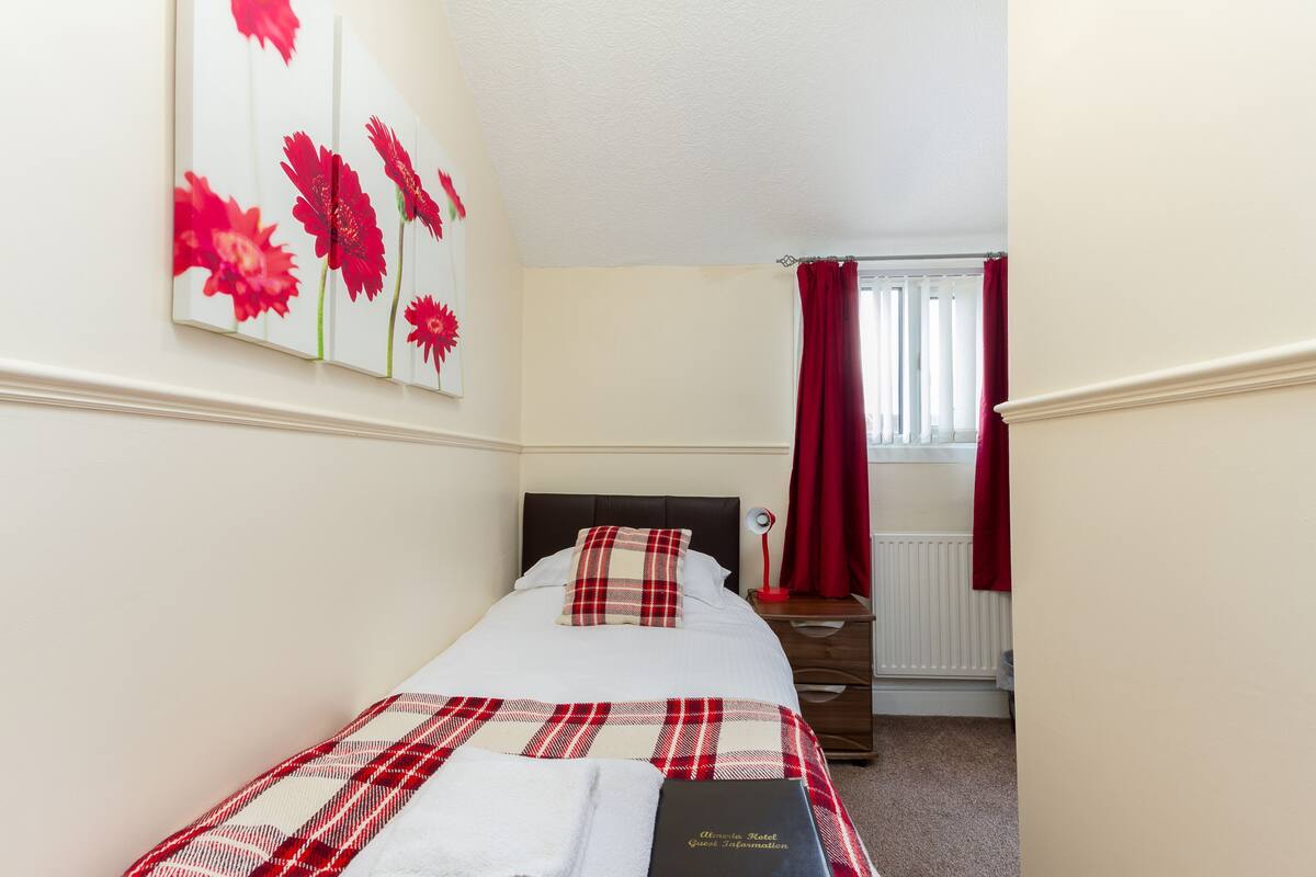 A neatly arranged bedroom with a bed, a bedside table, a lamp, and a window with curtains.