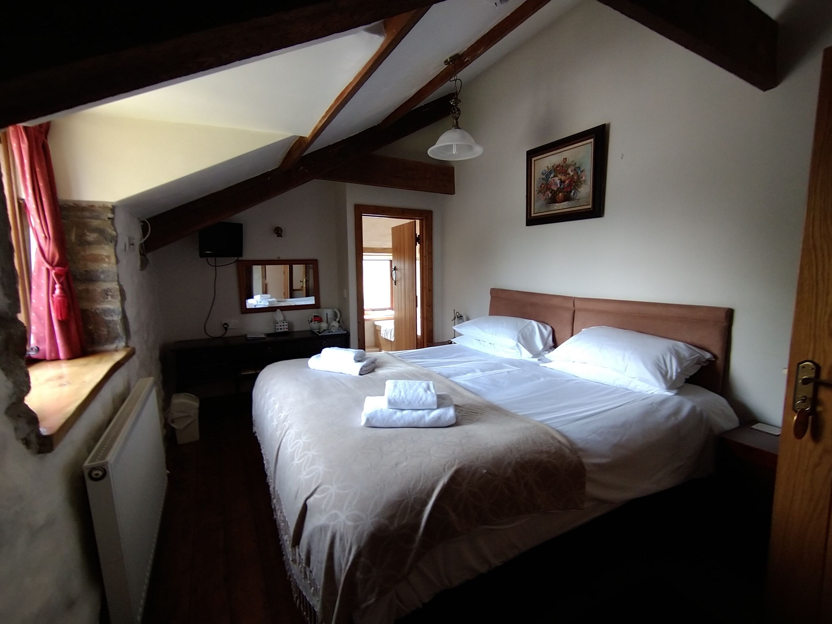 Une chambre à coucher avec un grand lit, des poutres apparentes, une commode, un miroir et un tableau au mur.