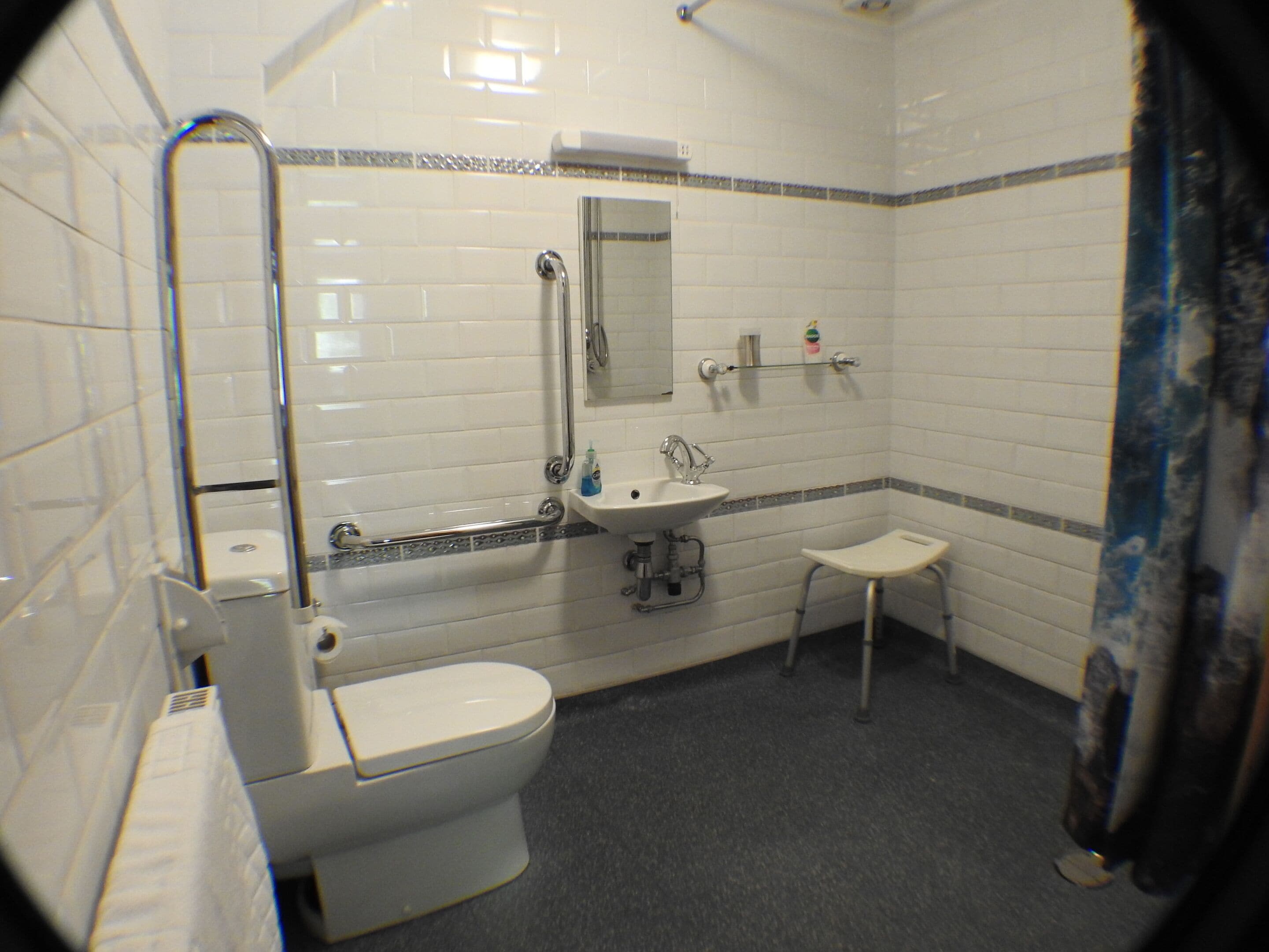 A bathroom with white tiled walls, a white toilet, a sink, and a shower area.