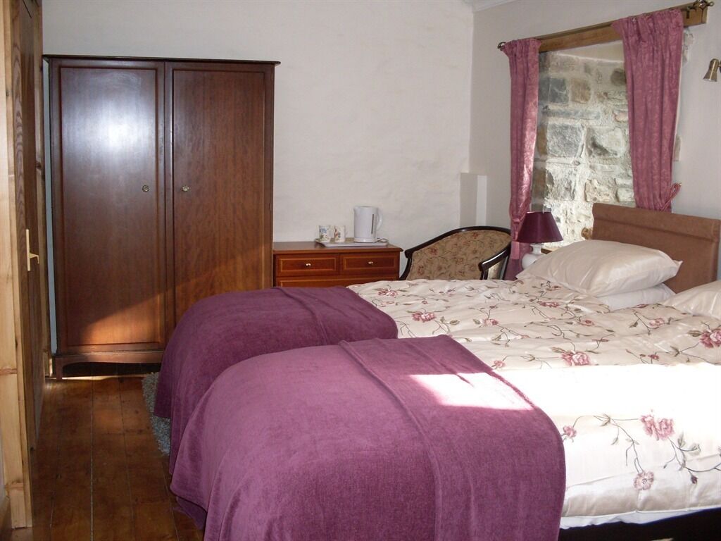 Un dormitorio con cama, armario, mesita de noche y ventana con cortinas.