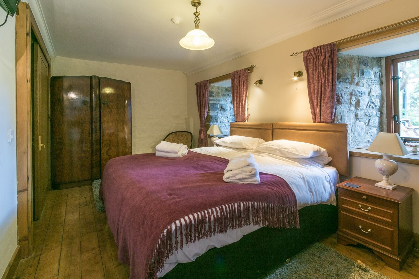 Un dormitorio con una cama grande, un armario de madera, una pared de piedra y una ventana con cortinas.